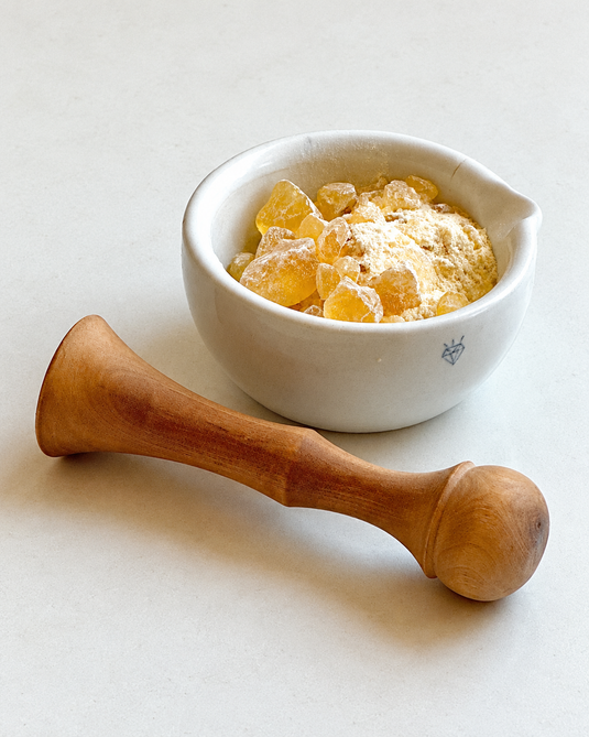 Golden pine rosin pieces and powder in a white mortar with a wooden pestle